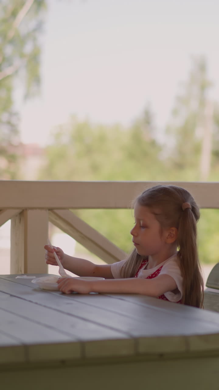 Little girl with lack of appetite picks in plate sitting with mother on terrace of hotel restaurant slow motion. Woman waits daughter in cafe. Dinner in public place
