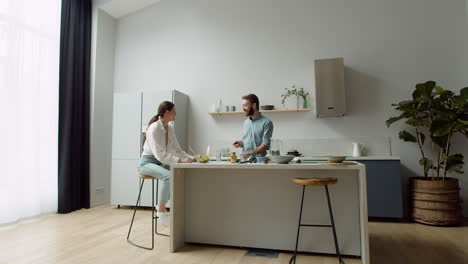 cheerful couple chatting about something funny while preparing a tasty salad in a modern kitchen