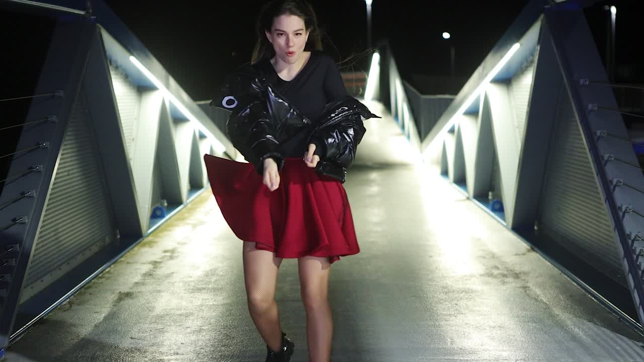 Happy and care free young female dancer performing at night on well lit bridge urban setting