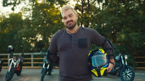 A-biker-with-white-hair-with-a-beard-and-an-earring-stands-and-holds-a-motorcycle-helmet-in-his-hand