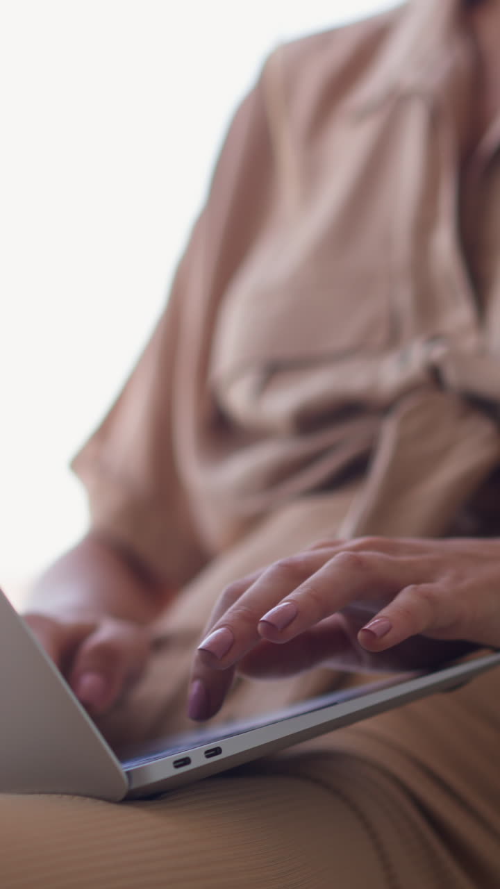 Young blonde woman in beige clothes types text for study on computer sitting near bright window in comfortable room at home slow motion