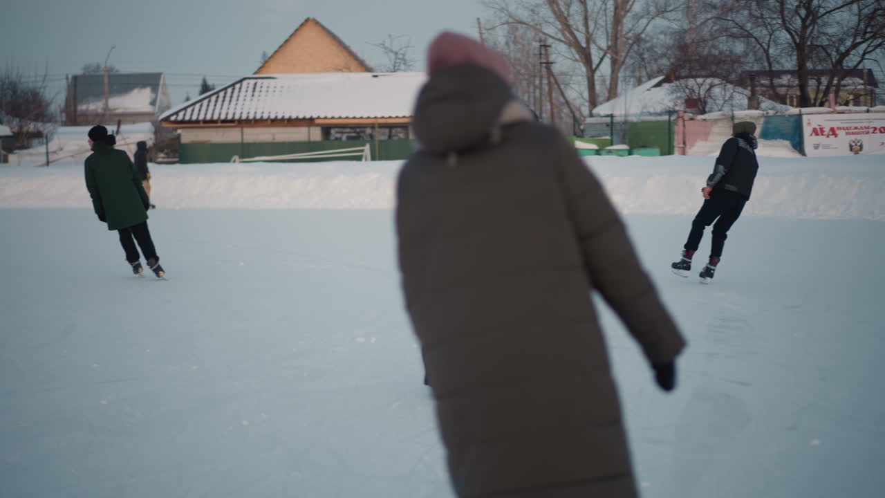 fellow skater watching boy skate skillfully on snow covered rink near icy banks and urban buildings, smooth gliding under pale winter sky capturing focused attention and graceful motion