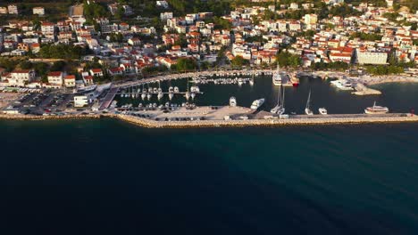 amazing aerial view flying forward into harbour during sunset in baska voda, croatia with mountains, boats and sea in 4k