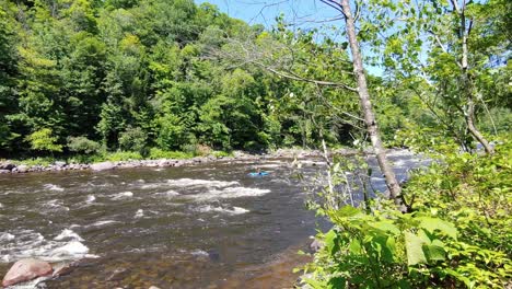 Kamerafahrt-Einer-Wunderschönen-Flusslandschaft-Mit-Kajakfahren-Im-Wasser-Mit-Der-Strömung-An-Einem-Sonnigen-Tag