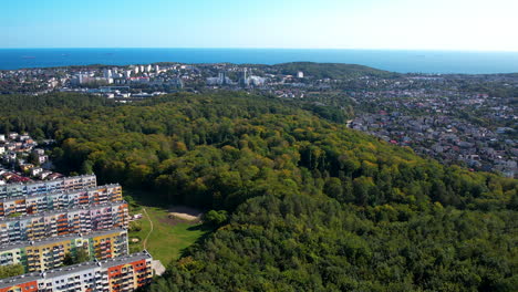 Aerial-backward-view---residential-district-in-Gdynia-with-a-view-of-the-Gdańsk-Bay---clear-sky-in-the-background,-green-trees-in-the-landscape-park,-housing-estate-close-to-the-forest,-natural-spaces