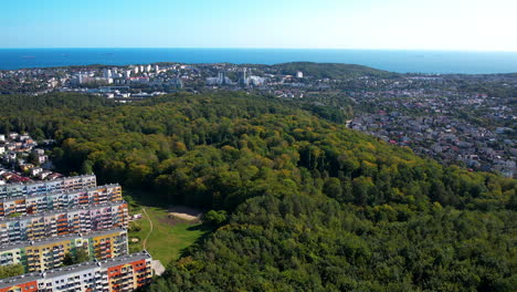 vista aérea hacia atrás - distrito residencial en gdynia con vista a la bahía de gdańsk - cielo despejado en el fondo, árboles verdes en el parque paisajístico, complejo de viviendas cerca del bosque, espacios naturales