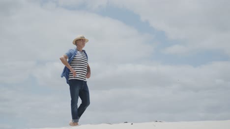 Happy-senior-caucasian-man-walking-barefoot-on-tropical-beach-and-raising-arms,-in-slow-motion