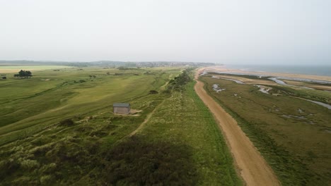 Drone-aerial-shot-of-Norfolk-coast-with-Golf-course,-marsh-land,-sand-dunes-and-sea-in-view-looking-out-to-Hunstanton-in-the-distance