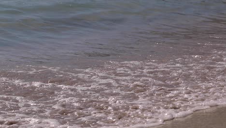 Slow-motion-shoot-of-sea-waves-moving-over-golden-sandy-beach-in-bright-sunshine