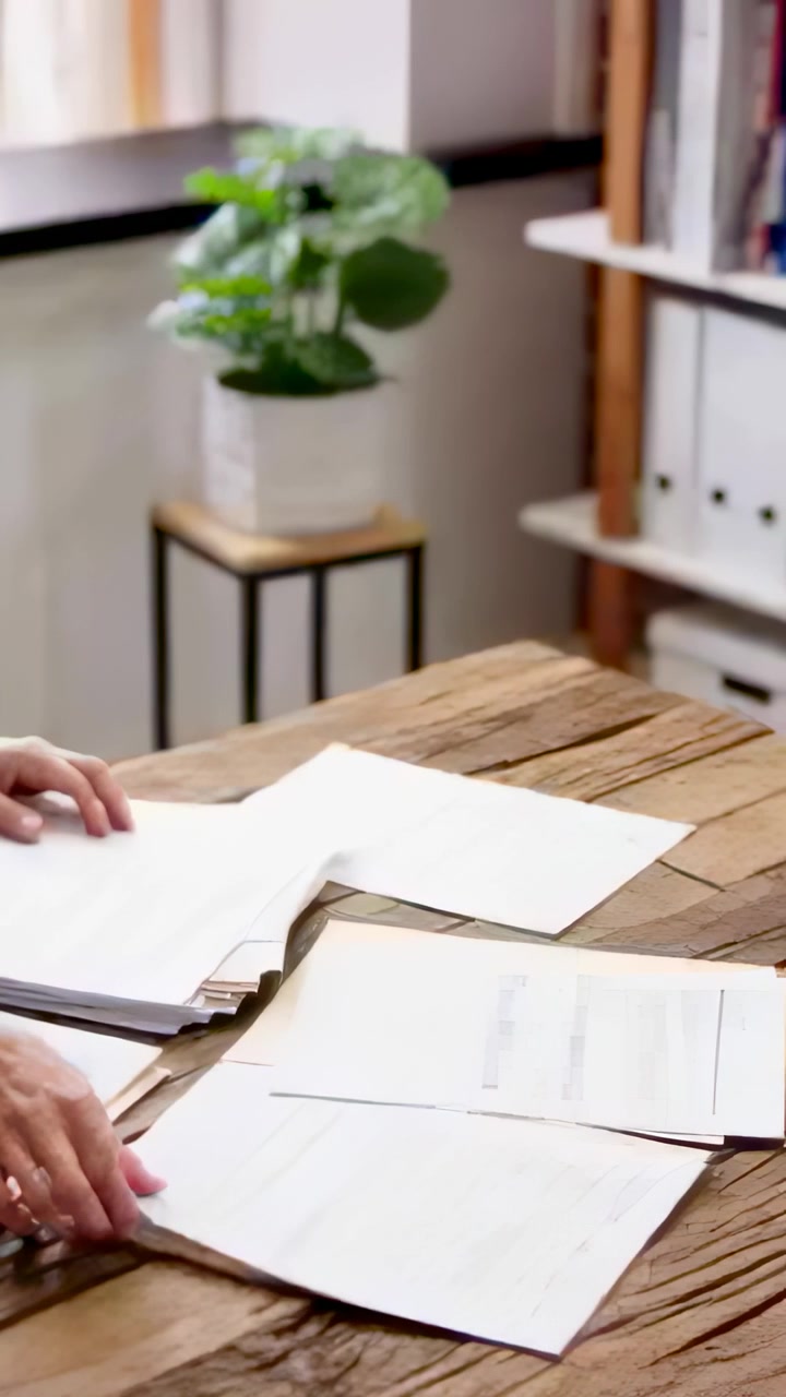 Vertical video: Placing stack, hands flipping and sorting papers at office desk, in light sleeve