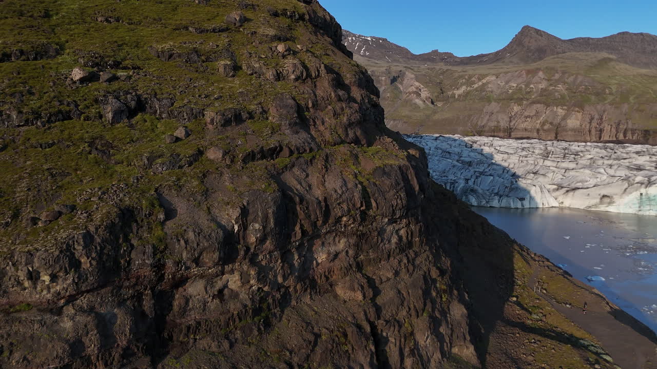 Aerial view of Svínafellsjökull Glacier at sunset, showing deep ice crevasses flowing into a dark glacial lagoon, framed by steep volcanic mountains and warm evening light in southern Iceland