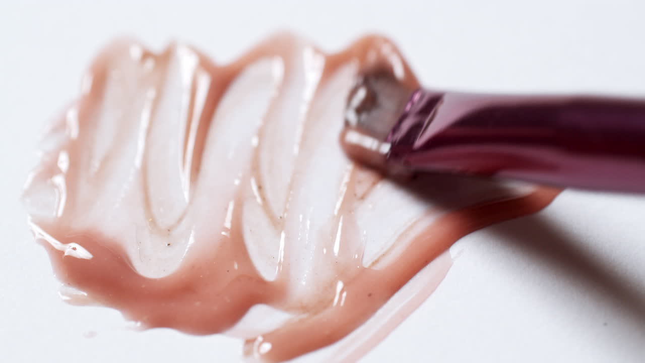 Smudging some glossy lip gloss, using a brush applicator on a plain-white board pallet