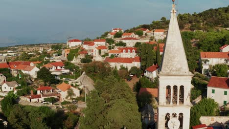 backward drone aerial near church bell tower reveals nerezisce village and church facade on brac island, croatia