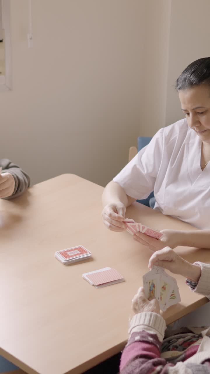 Senior people and caregiver playing cards in a nursing home