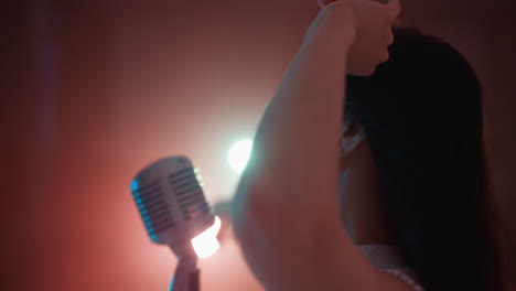 primer plano de una cantante con un vestido blanco y un micrófono vintage, en un fondo rosado. su cabello se mueve y las manos están en movimiento