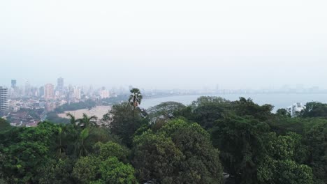 A-cinematic-drone-shot-of-the-famous-Marine-Drive-Chaupati-Beach-point-in-South-Bombay-region-of-Mumbai-City,-overlooking-the-hanging-garden-hill-and-forest-in-a-slow-smooth-motion