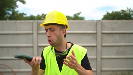 Un-Trabajador-De-La-Construcción-Que-Lleva-Un-Casco-Amarillo-Está-Enfrascado-En-Una-Acalorada-Conversación-Con-Alguien-Por-Teléfono---Primer-Plano-Medio