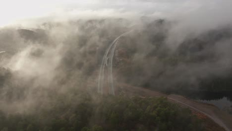 drone footage of highway, and housing estate in norway with some fog floating in the air and sun lighting up the clouds