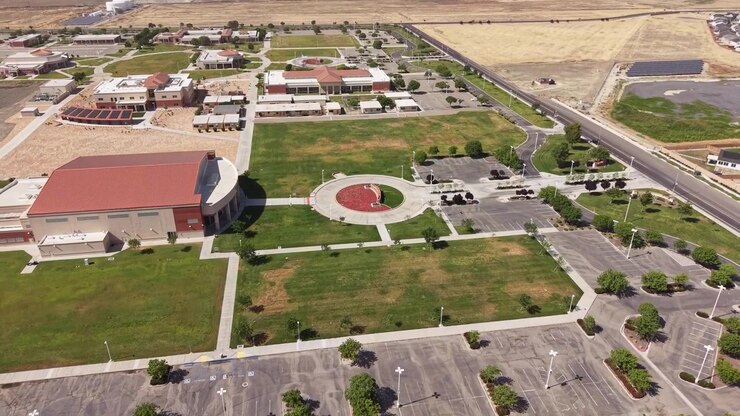 Riprese aeree con drone in ascesa che sorvolano il campus del Lemoore College, mostrando i moderni edifici universitari, prati verdi e ampi parcheggi vuoti in una giornata di sole nella California Centrale