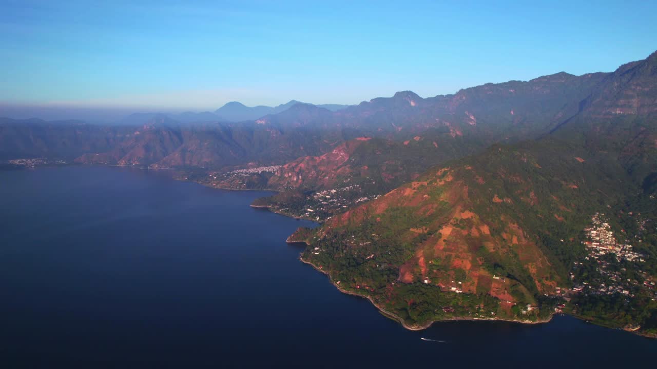 Ripresa panoramica a sinistra con drone lungo la costa del lago di Atitlán che rivela montagne, villaggi e terreno texturizzato alla luce del giorno