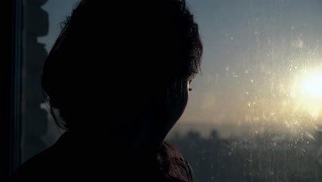 girl stands and looks at sunset near window close view