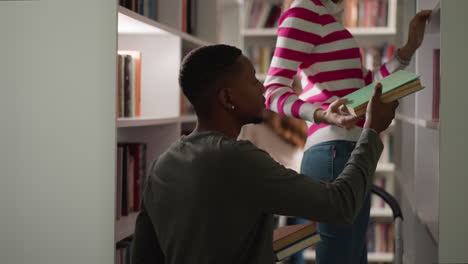 black man takes books from girl friend in library. young woman standing on step ladder reaches folio to guy in bookstore. students choose textbooks