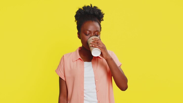 Donna afroamericana che si gusta il caffè del mattino in un bicchiere di plastica, con espressione soddisfatta