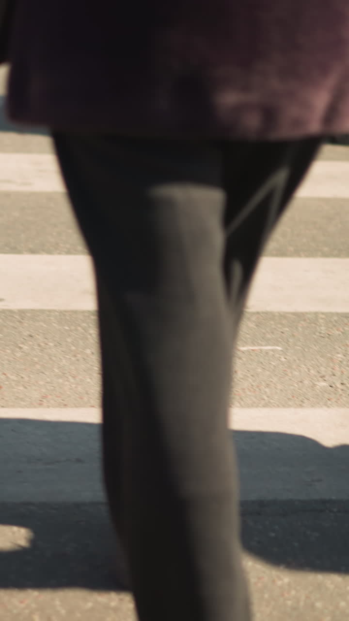 pedestrians crossing city street, closeup legs and shadows brisk morning commute with office worker, courier, student and shopper passing through intersection, shoes tapping asphalt, signal timing