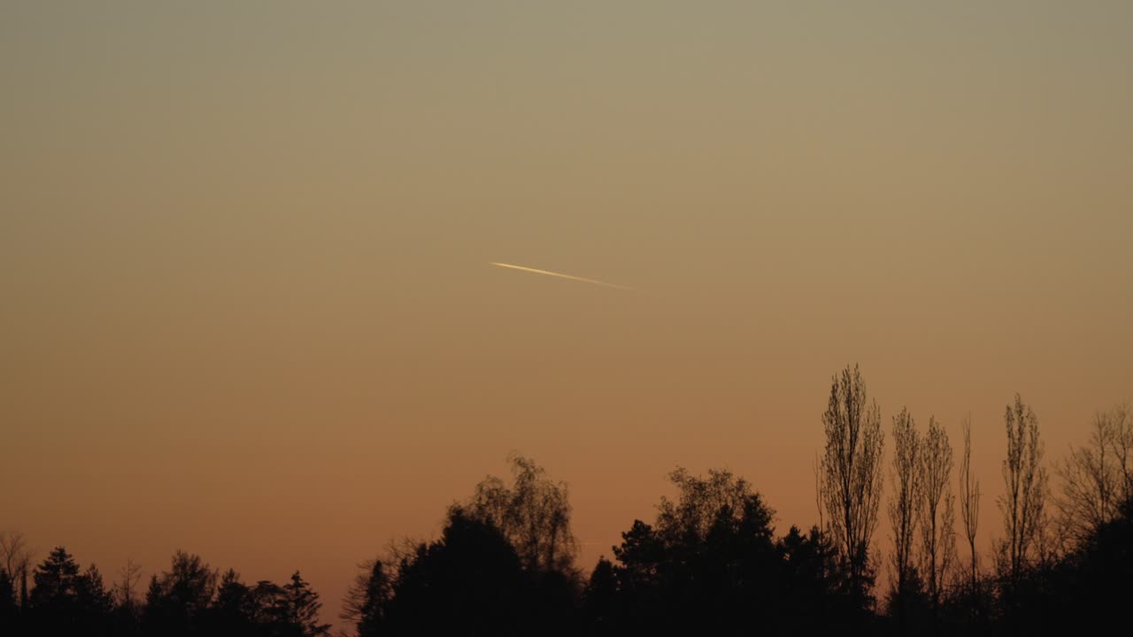 Scia di condensazione persistente lasciata da un aereo ad alta quota illuminata dal sole durante il tramonto