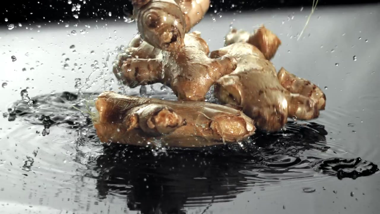 Fresh Ginger Roots Falling into Water with Splashes in Slow Motion