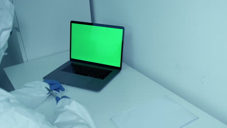 hospital worker in protective scrubs gestures and points to green screen laptop notes