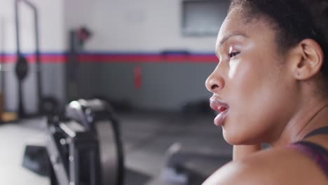 Video-Einer-Müden-Afroamerikanerin-Auf-Einem-Rudergerät,-Die-Sich-Nach-Dem-Training-Im-Fitnessstudio-Erholt