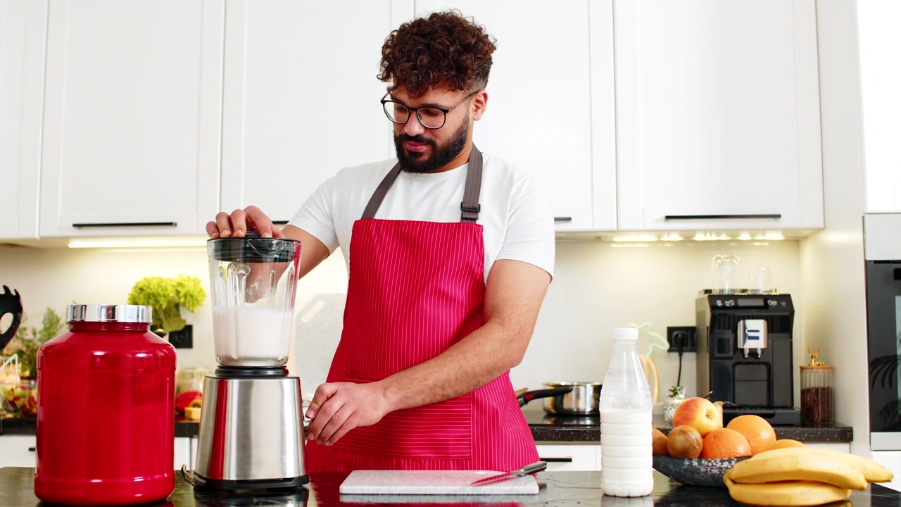 Giovane adulto arabo che frulla un frullato di proteine del siero del latte con banana e mela per il fitness nella cucina di casa