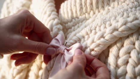 close-up of hands attaching a pink satin bow to a cream cable-knit fabric