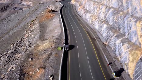 las maravillas de las imponentes montañas en jebel jais emiratos árabes unidos con un vehículo que viaja en la carretera junto a acantilados erosionados durante el día - toma aérea