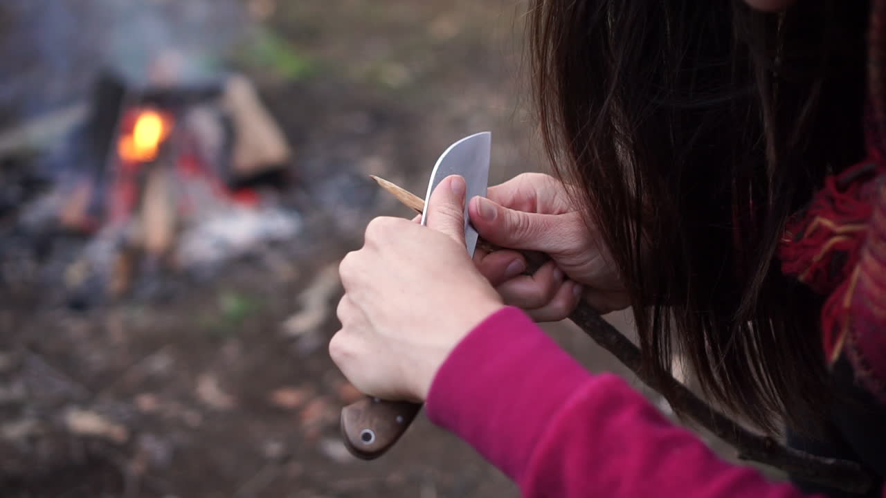 mujeres caucásicas con cabello largo, lanza tallada con cuchillo, fondo de fogata, plano medio