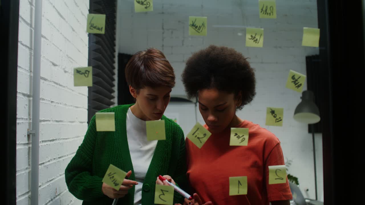 Two women collaborate, brainstorming ideas on a glass wall