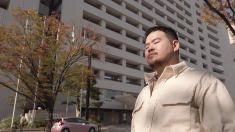 asian-man-using-smart-mobile-phone-texting-chatting-or-looking-for-maps-while-walking-in-the-city-of-Japan-in-autumn-time-under-clear-blue-sky,-asian-tourist-business-man-use-phone-in-60p-video