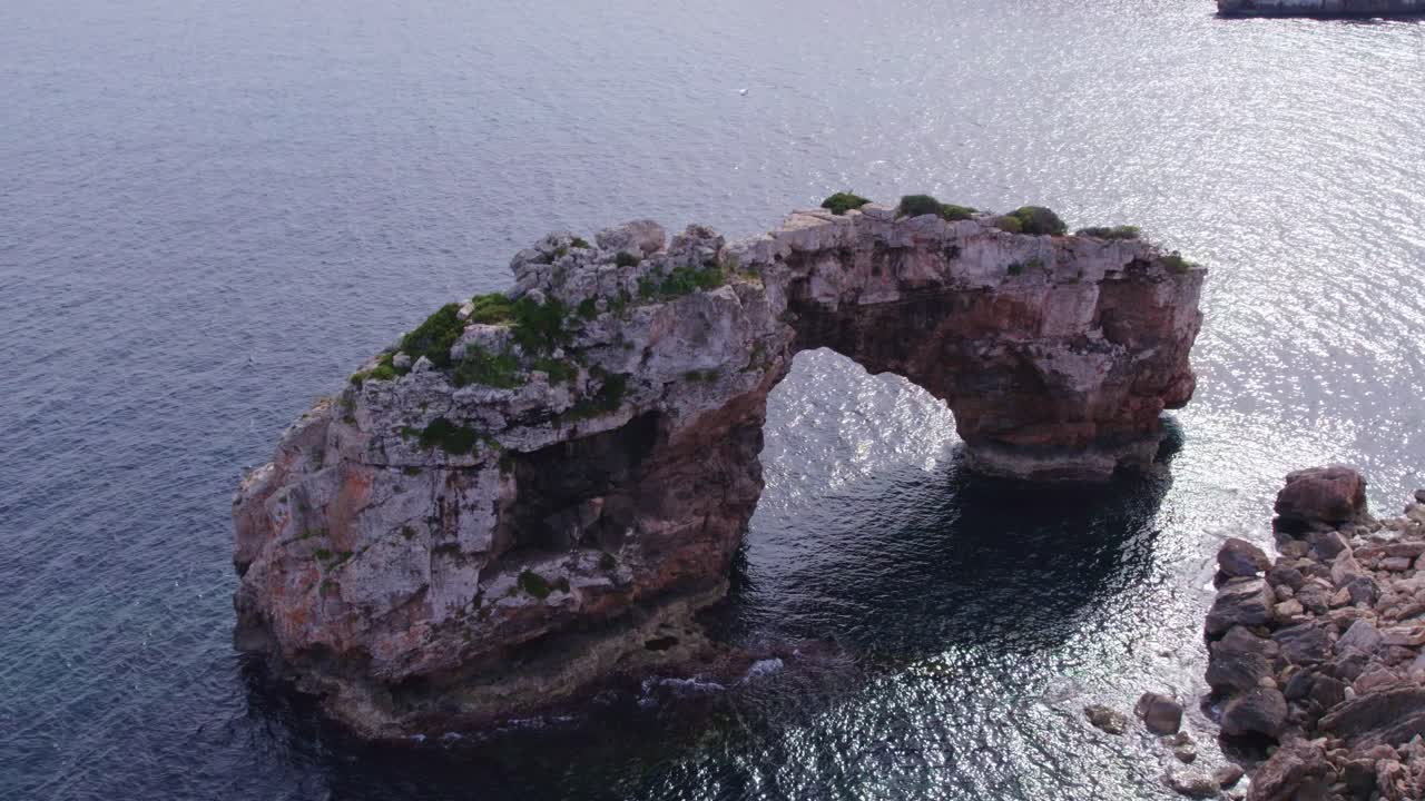 Side panning shot of Es Pont&agrave;s natural arch Mallorca during day time, aerial