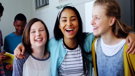 niñas escolares sonrientes de pie con los brazos alrededor en el corredor