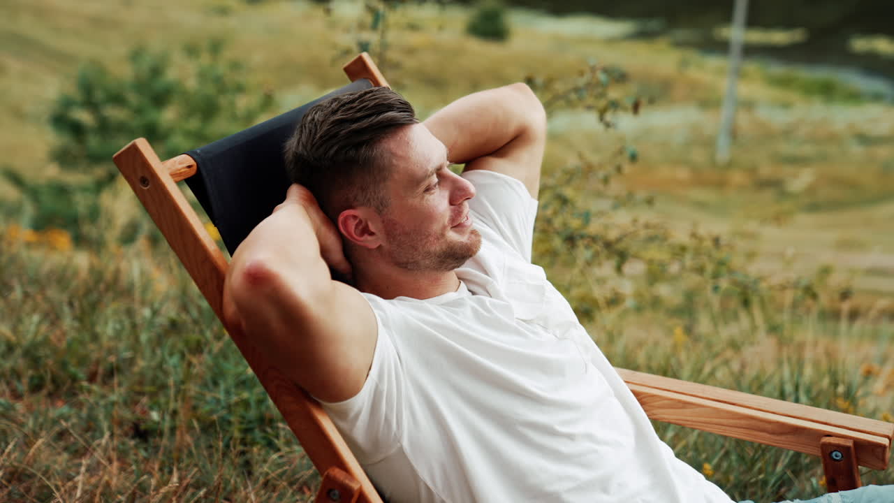 Caucasian man enjoying rest in the nature. Man sits comfortably in a folding chair, looking around.