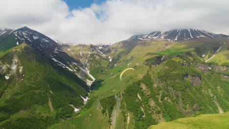 drone shot of the caucasus mountains with a paraglider entering the frame from the left