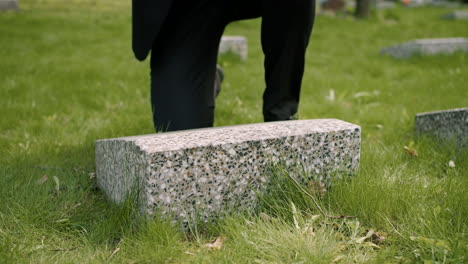 close up view of unrecognizable man in black suit cleaning a tombstone with a handkerchief in a graveyard