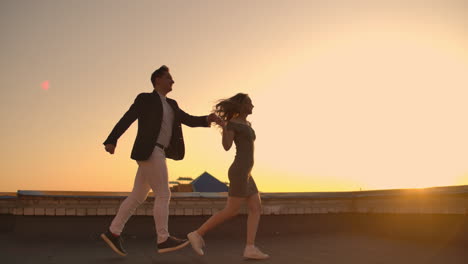 cute lovers laughing running on the roof of the building at sunset on the background of the city and hugging standing at the edge. romance and love