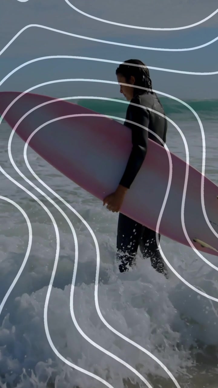Video verticale: Un surfista individua un'onda, con la sua tavola rosa, mentre cammina verso il mare tenendo la tavola per fare sport.