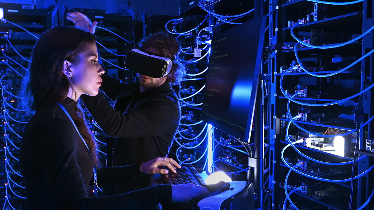Woman programming in a server room while a man is using a Virtual Reality headset