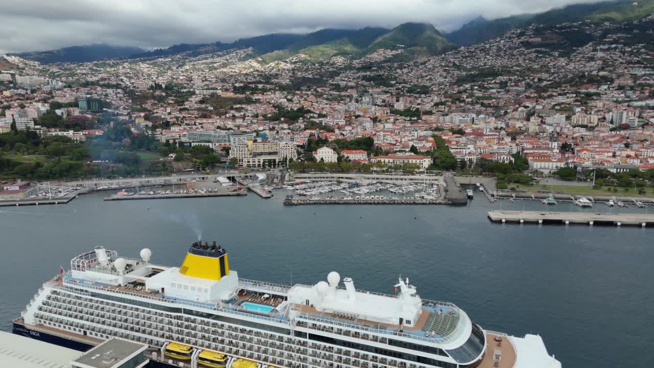 Drone shot flying over large cruise ship docked at port in coastal tourist city