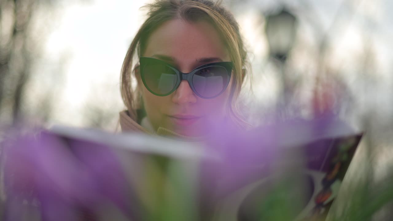 Brunette woman in brown coat reading a book at a terrace