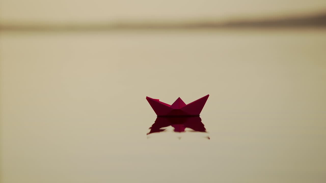 Red Paper Ship in the river. Origami Paper Boat is Sailing in the lake. Beautiful Waves Ripple Background. Unusual Travel Concept. Filtered video.