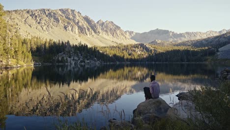 person sitting on rock by calm lake with mountain reflection